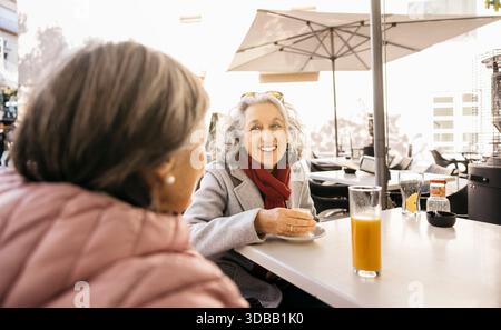 Ältere Freundinnen sitzen in einem Café im Freien, lächeln und reden Stockfoto