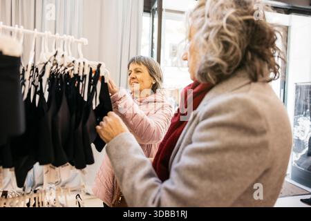Zwei Seniorenfreunde, die in einem Regal in einer hellen Boutique ihre Kleidung durchsuchen Stockfoto