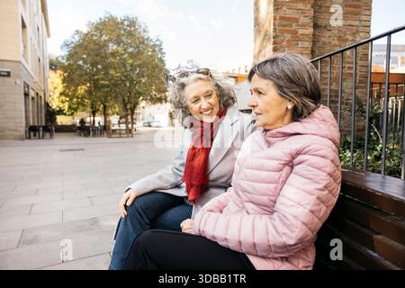 Zwei ältere Freundinnen sitzen auf einer Bank und unterhalten sich im Freien Stockfoto