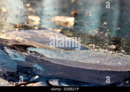 Transparente Eisplatten auf gefrorener Flussoberfläche, beleuchtet durch Wintersonne. Natürliche kalte Texturen und saisonale Atmosphäre Stockfoto