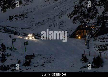 Ein Pistenfahrer überquert nachts eine gewundene Bergstraße in Obertauern, Österreich. Die Szene wird von den Scheinwerfern und den Lichtern des Putzers beleuchtet Stockfoto