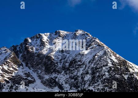Ein atemberaubender Blick auf einen schneebedeckten Berggipfel, der majestätisch gegen einen leuchtend blauen Himmel ragt. Das zerklüftete Gelände steht im Kontrast zu den Stockfoto