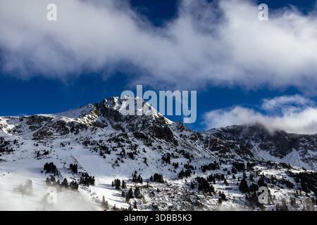 Ein atemberaubender Blick auf einen schneebedeckten Berggipfel unter einem dramatischen Himmel voller flauschiger weißer Wolken. Die Berghänge sind mit tiefem Schnee bedeckt, wi Stockfoto