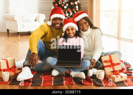 Die Familie trägt Santa Hats und sitzt während der Feiertage zusammen auf dem Boden in einem gemütlichen Wohnzimmer Stockfoto