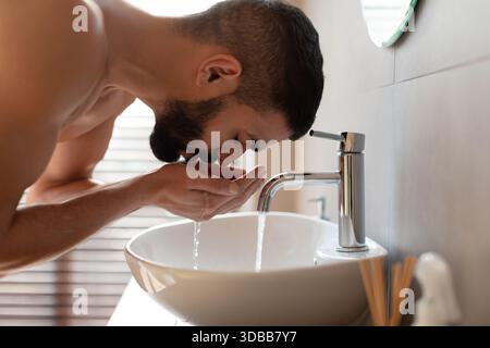 Muskulöser Mann, der morgens Hautpflege-Routine durchführt, während er sein Gesicht im Bad wäscht Stockfoto