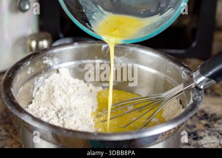 Die Mischung aus flüssigem Ei, Milch und Öl wird vorsichtig in eine silberne Schüssel in die trockenen Zutaten gegeben, um die endgültige Herstellung des Waffelteigs zu beginnen Stockfoto