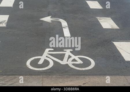 Der Blick auf ein weißes Fahrradsymbol und einen Linkspfeil auf dem dunklen Asphalt eines Radwegs schaffen einen starken Kontrast, Indre by, Dänemark. Stockfoto