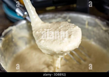 Eine Kelle hebt einen dicken, cremigen Messlöffel mit glattem Waffelteig aus der Schüssel, der auf das heiße Bügeleisen in Waukesha County gegossen werden kann. Stockfoto