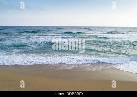 Aus der Vogelperspektive der türkisfarbenen Wellen, die sanft den goldenen Sand unter einem weichen Himmel küssen, Vrachos, Preveza, Griechenland. Stockfoto
