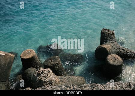 Klares, türkisfarbenes Meerwasser, das gegen alte Holzpfähle oder Bruchwasserreste am Ufer wäscht. Stockfoto