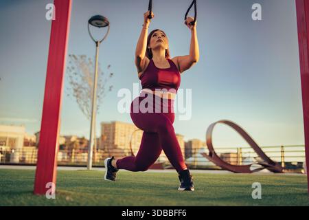Tiefwinkelansicht einer jungen Frau bei Hängeübungen mit Straps. Weibliches Fitness-Modell beim Beintraining bei Sonnenuntergang. Stockfoto
