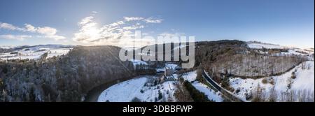 Blick aus der Vogelperspektive auf Neidpath Castle, eingebettet in ein schneebedecktes Tal, mit dem Fluss Tweed, der sich durch mattierte Bäume unter einem klaren Winterhimmel schlängelt. Stockfoto
