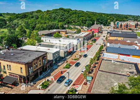 Blick aus der Vogelperspektive auf die Innenstadt von Algonquin, Illinois, mit historischen Gebäuden der Main Street, Verkehr, Gehwegen und üppigen grünen Hügeln an einem hellen Tag. Stockfoto