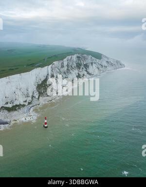 Blick aus der Vogelperspektive auf die Kreidefelsen von Beachy Head, die auf das türkisfarbene Meer treffen, mit dem berühmten rot-weißen Leuchtturm, Eastbourne, Vereinigtes Königreich Stockfoto