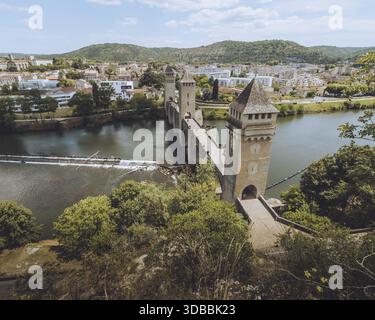 Blick auf die Steintürme des Pont Valentré, die stark über dem ruhigen Lot River stehen, ein mittelalterliches Wunder unter dem hellen Himmel, Cahors, Occitanie, Franc Stockfoto