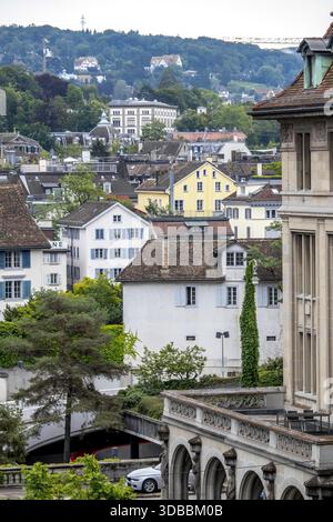 Blick auf Gebäude mit vielfältiger Architektur, von weißen Wänden mit blauen Fensterläden bis zu kunstvollen Steinstrukturen, eingebettet in üppiges Grün, Zuri Stockfoto