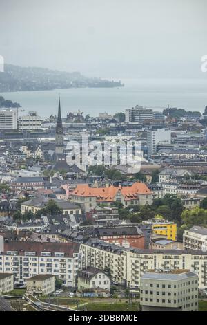 Blick auf die Gebäude mit bunten Dächern, die bis zum Wasserrand kaskadieren, einen Kathedralenturm, der die Skyline über der Stadtlandschaft durchzieht, Zürich, Switz Stockfoto
