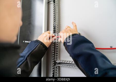 Die Hände eines Elektrikers führen einen roten Draht durch einen Kabelkanal auf einer weißen Platte Stockfoto