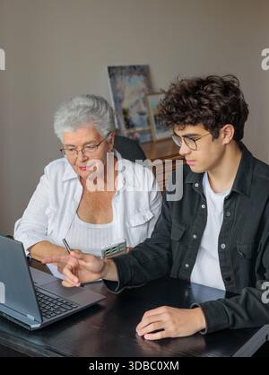 Großmutter und Enkel nutzen ihr Notebook zu Hause gemeinsam für Online-Banking, Rechnungszahlungen, Reisebuchungen und das Erlernen digitaler Fähigkeiten. Familienunterhalt, Stockfoto
