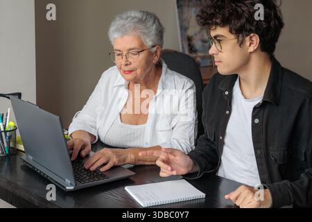 Großmutter und Enkel nutzen ihr Notebook zu Hause gemeinsam für Online-Banking, Rechnungszahlungen, Reisebuchungen und das Erlernen digitaler Fähigkeiten. Familienunterhalt, Stockfoto