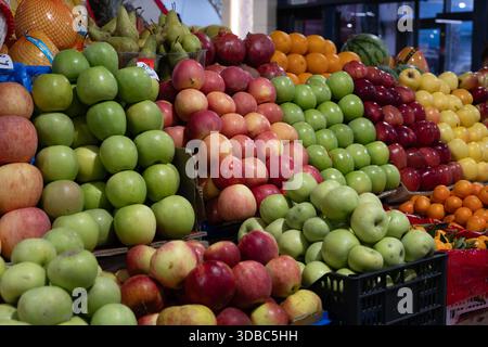 Farbenfrohe Pyramiden mit frischen Äpfeln in verschiedenen Grün-, Rot- und Gelbtönen, mit Orangen, Granatäpfeln und Birnen an einem Obstmarkt. Stockfoto