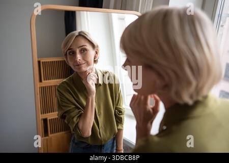 Schöne lächelnde Frau mittleren Alters, die Spiegelreflexe mit positivem, zufriedenem Ausdruck betrachtet. Stockfoto