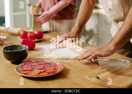 Junger Erwachsener Mann, Der Teig Rollt, Während Frau Käse Reißt Stockfoto