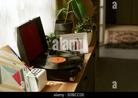 Vintage-Plattenspieler, der Vinyl neben gerahmtem Foto auf Holzschrank dreht Stockfoto