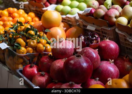 Ein lebhafter Marktstand bietet Granatäpfel im Vordergrund, begleitet von Mandarinen, Orangen, Grapefruits und einer Vielzahl von grünen und roten Äpfeln Stockfoto