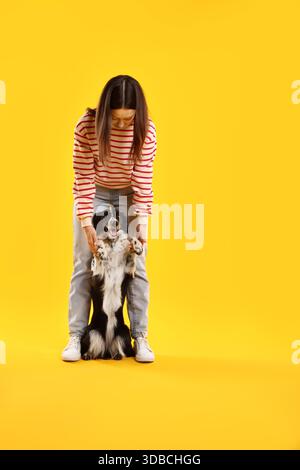 Frau mit ihrem süßen Border Collie Hund auf gelbem Hintergrund, Platz für Text Stockfoto