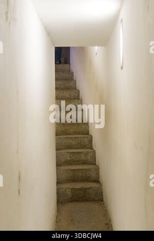 Eine enge Steintreppe führt durch einen schmalen Korridor nach oben und betont den engen Raum und die raue architektonische Struktur Stockfoto