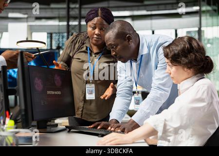 Die junge Ingenieurin im Büro bittet Kollegen um Hilfe, um das Eindringen von Hackern zu verhindern. Interne Unterstützung durch IT-Mitarbeiter bei der Koordination von Vorfallsreaktionen bei Netzwerk-ddos-Angriffen Stockfoto