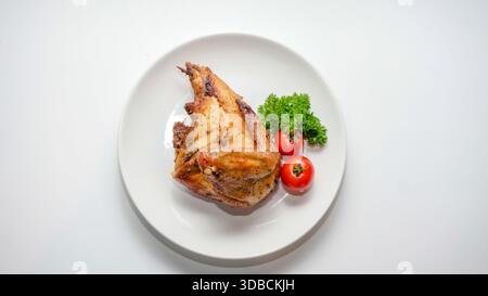 Gebratenes Hähnchenviertel serviert mit Kirschtomaten und Petersilie auf weißem Teller, isoliert auf weißem Hintergrund Stockfoto