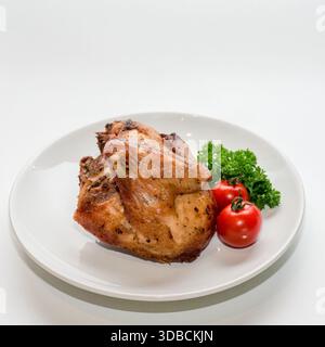 Gebratenes Hähnchenviertel serviert mit Kirschtomaten und Petersilie auf weißem Teller, isoliert auf weißem Hintergrund Stockfoto