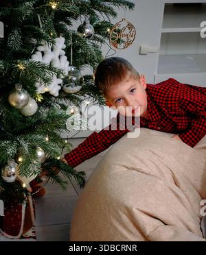 Fröhlicher Junge Bewundert Weihnachtsdekorationen Und Geschenke In Cozy Home Stockfoto