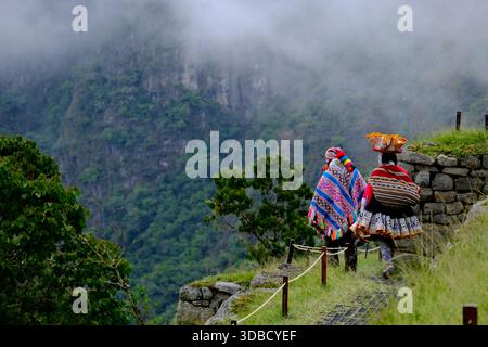 Zwei Frauen in traditioneller peruanischer Kleidung, die durch die nebelige Machu Picchu Landschaft laufen Stockfoto