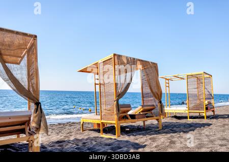 Liegestühle und Strohschirme am Strand von Santorin, Griechenland, bieten Entspannung für Sommerreisende. Stockfoto