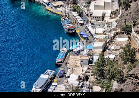 Aus der Vogelperspektive auf den alten Hafen von Fira (Skala) unterhalb der Stadt Fira, Santorin, mit Ausflugsbooten und der tiefblauen Ägäis, Griechenland. Stockfoto