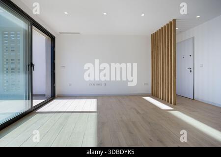 Helles leeres Zimmer mit Holzlamellen, großer Schiebetür und hellem Holzfußboden Stockfoto