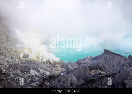 Wunderschöner einsamer Baum am Rand des Vulkans ijen (Kawah Ijen) mit blauem Säuresee und Schwefelgas aus dem Krater bei Sonnenaufgang, Java indonesia Stockfoto