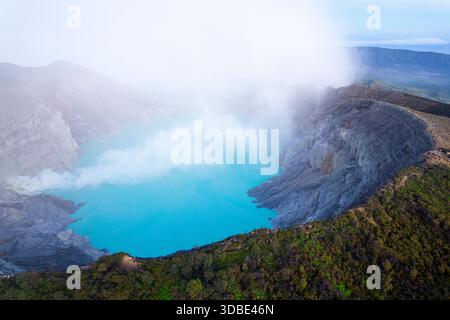 Spektakulärer Vulkan Ijen auf der Insel Java in Indonesien, Blick aus der Vogelperspektive auf einen Vulkankrater und einen blauen vulkanischen See mit dampfenden Lüftungsöffnungen bei Sonnenaufgang Stockfoto