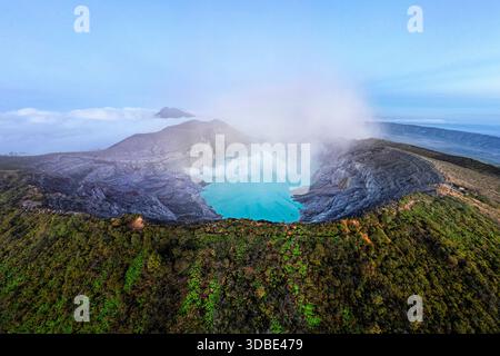 Spektakulärer Vulkan Ijen auf der Insel Java in Indonesien, Blick aus der Vogelperspektive auf einen Vulkankrater und einen blauen vulkanischen See mit dampfenden Lüftungsöffnungen bei Sonnenaufgang Stockfoto