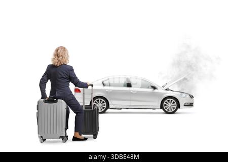 Rückansicht einer Frau, die auf einem Koffer sitzt und ein Auto mit offener Kapuze auf weißem Hintergrund betrachtet Stockfoto