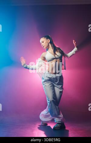 Porträt einer jungen Frau in voller Länge, die im Neon-Jazz-Funk-Hip-Hop-Stil mit blauem und rosafarbenem Licht für Nachtclub und Tanzwerbung posiert Stockfoto