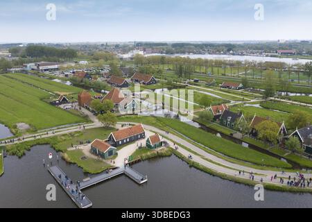 Blick aus der Vogelperspektive auf malerische grün-braune Häuser mit roten Dächern, eingebettet zwischen Kanälen und Feldern in der Nähe von Zaanse Schans, Zaandijk, Zaandam, Niederlande. Stockfoto