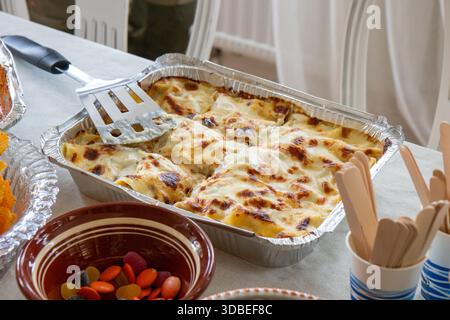 Gebackene italienische Lasagne wird auf einem Tisch unter anderen Feiertagsgerichten serviert. Hausgemachtes, komfortables Essen mit Nudelschichten, Käse und Soße, das ein fest unterstreicht Stockfoto