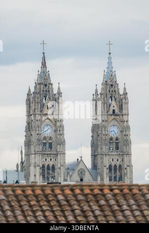 Blick auf die kunstvollen Türme einer gotischen Kathedrale, die den bewölkten Himmel hinter einer traditionellen roten Dachlinie in Quito, Ecuador., Quito, Ecuador. Stockfoto