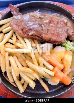 Lendensteak in mittelseltener Pilzsauce, Pommes Frites, Gemüse auf einer heißen Platte, damit es heiß bleibt. Vertikale Ansicht. Köstlich aussehende Mahlzeit. Stockfoto
