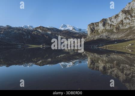 Blick auf das ruhige Wasser, das die schneebedeckten Berge unter einem klaren blauen Himmel spiegelt und die zerklüfteten Klippen in Lagos de Covadonga, Cangas de widerspiegelt Stockfoto