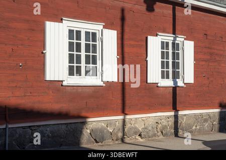 Blick auf ein rustikales rotes Holzgebäude mit hellen weißen Fensterläden, beschattet von einem Stab, auf einem Steinfundament, Karlskrona, Blekinge County Stockfoto